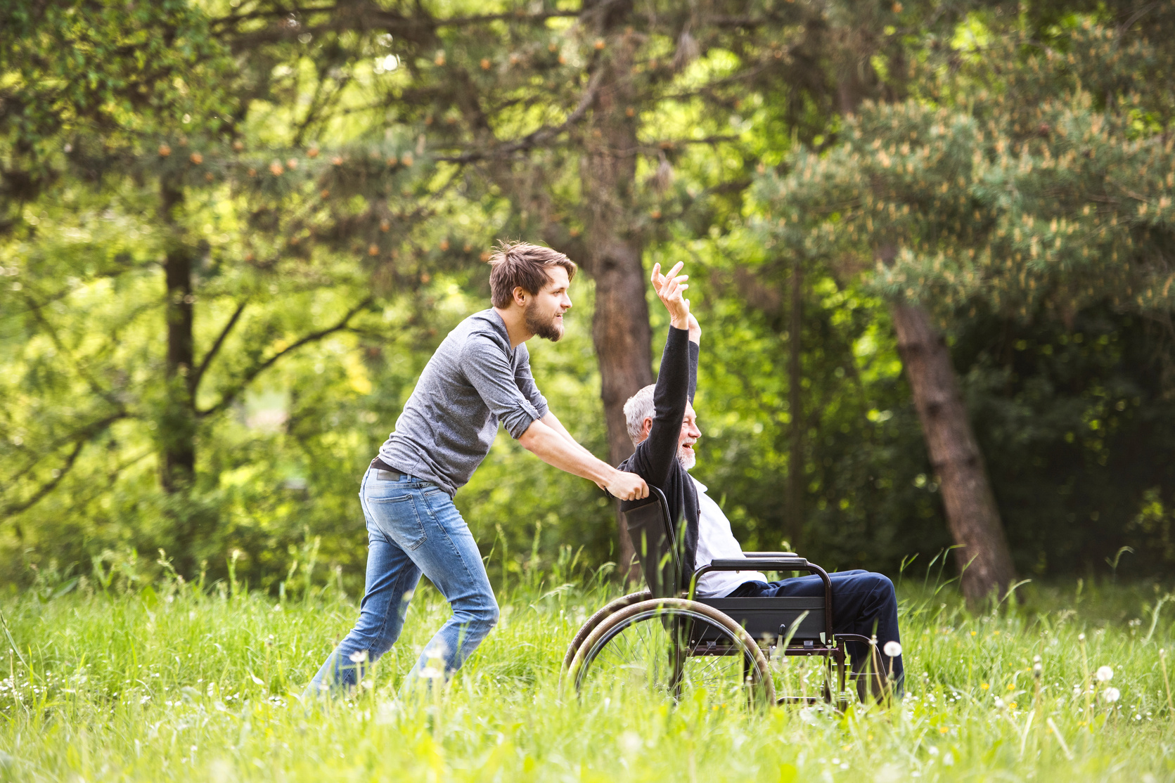 Hipster Son Walking with Disabled Father in Wheelchair at Park